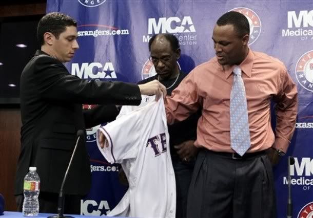 Texas Rangers general manager Jon Daniels, left, and manager Ron Washington, rear, assist newly-acquired third baseman Adrian Beltre, right, with his new team jersey following a baseball news conference announcing Beltre's acquisition, Wednesday, Jan. 5, 2011, in Arlington, Texas.