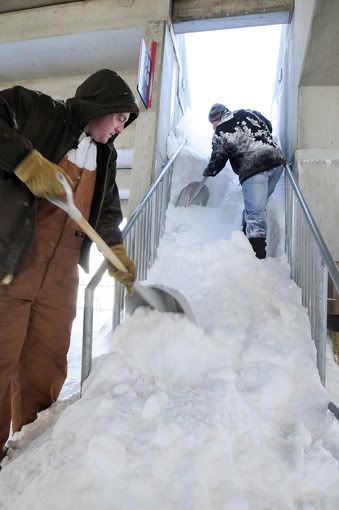 Brian Datri, left, of Troy, N.Y., and Eric Docchio of Waterbury, volunteers from Teen Challenge, clear a cascade of snow from a stairway at Rentschler Field in East Hartford on Friday. 
